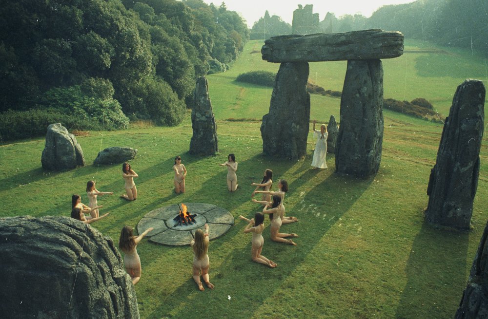 screencap from the Wicker Man; a circle of kneeling, naked women around a fire in a stone circle